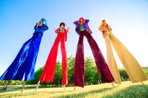 Young people on stilts posing against the blue sky.