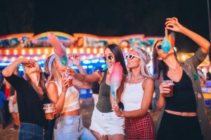 Female friends eating cotton candy and drinking beer in amusement park